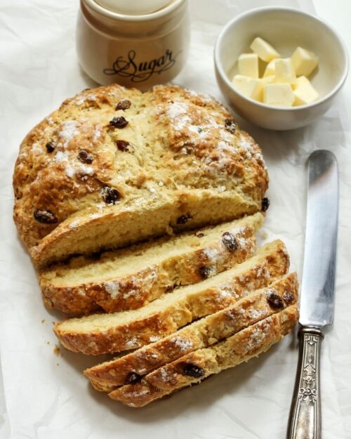 irish soda bread on a cutting board with a knife and bowl of butter. 