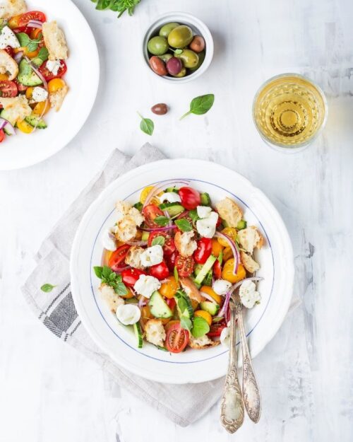 panzanella bread salad in a white bowl with sliced tomatoes, cheese, and fresh basil. 