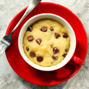chooclate chip cookie in a mug on a red plate with a fork.