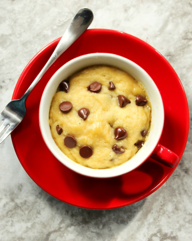 chooclate chip cookie in a mug on a red plate with a fork. 