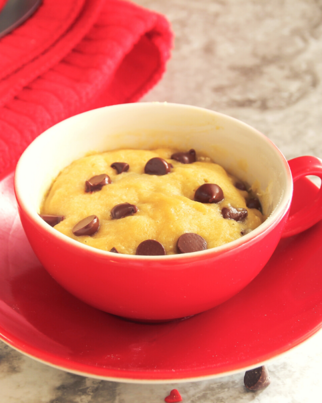 Up Close photo of a chocolate chip cookie in a red mug with chocolate chips on top. 