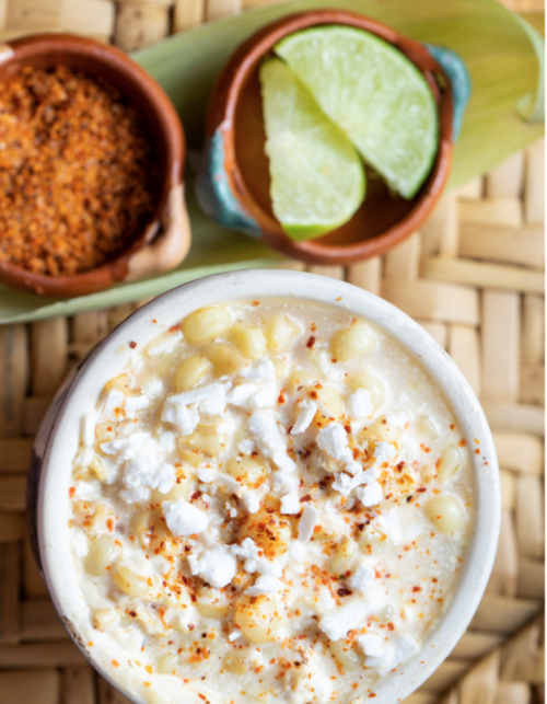 creamy elote in a white mug with limes.