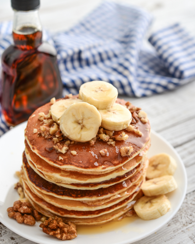 Pancakes stacked with bananas and walnuts on a white plate.