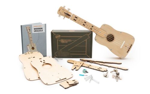Disassembled wooden ukulele parts alongside an assembled ukulele and packaging box