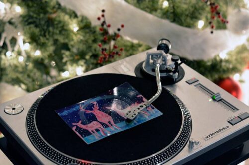 A turntable playing a festive vinyl postcard, surrounded by twinkling holiday lights and decorative garland.